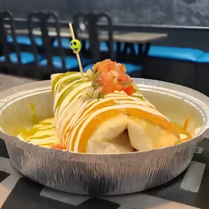 A large burrito from Tamales Inc. drizzled with green and orange sauces, topped with pico de gallo.
