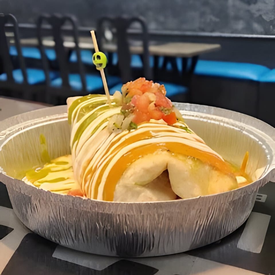 A large burrito from Tamales Inc, topped with salsa, green and orange sauces, in a foil container.