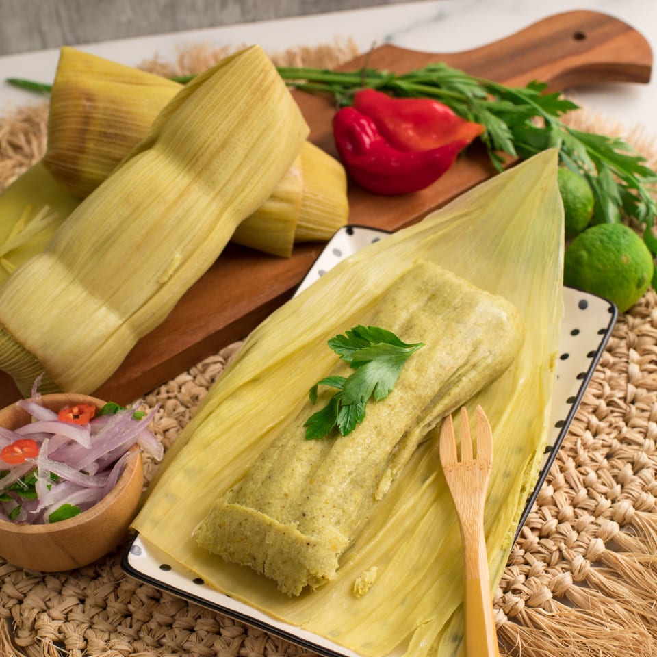Tamales Inc's green tamale, garnished with parsley, on a plate with red onions and peppers.